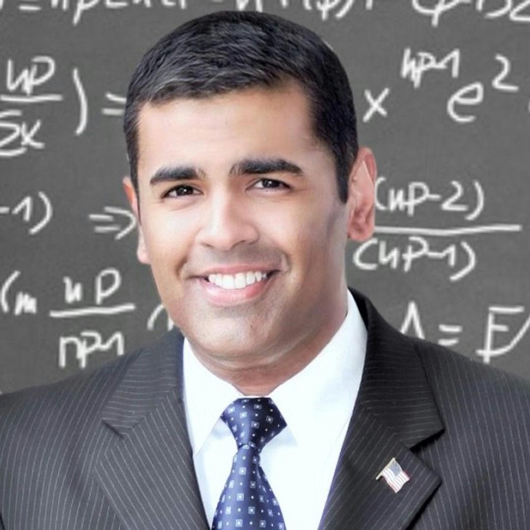 Michael Sury, dressed in a suit and tie, with a blackboard background