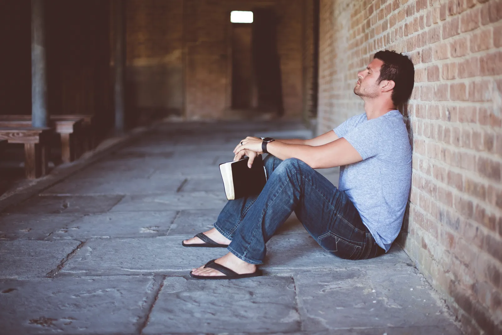 A man sitting on the ground and leaning on a wall with eye closed