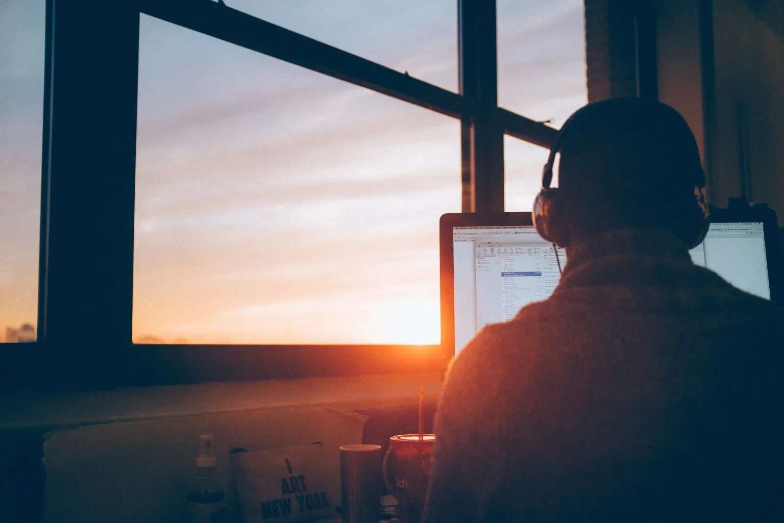 Man at desk with headset in front of computer with sunrise in window 