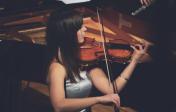 Woman practicing with a violin next to a grand piano.