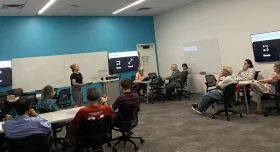 A diverse group of individuals sitting in chairs in a classroom, engaged in a learning environment.