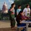 A Group of female students work on computer-based problems with an instructor at the base of the UT Tower, the Texas Capitol looms in the distance.