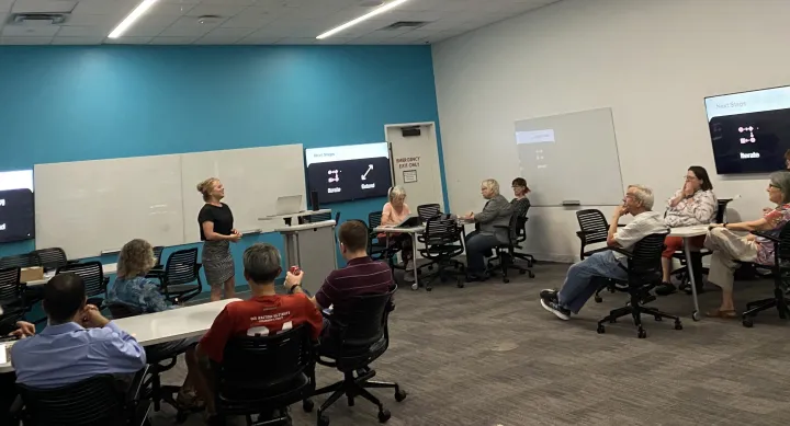 A diverse group of individuals sitting in chairs in a classroom, engaged in a learning environment.