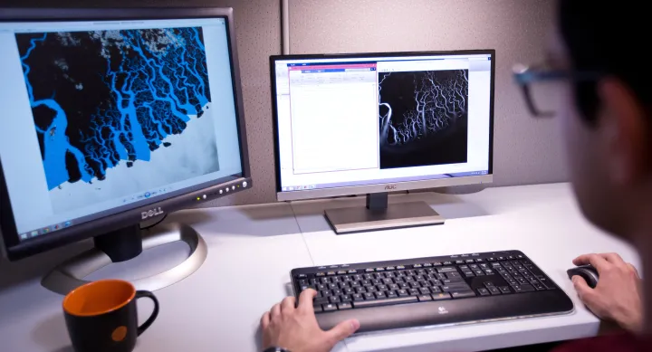 Computer screens and a keyboard with hands on it