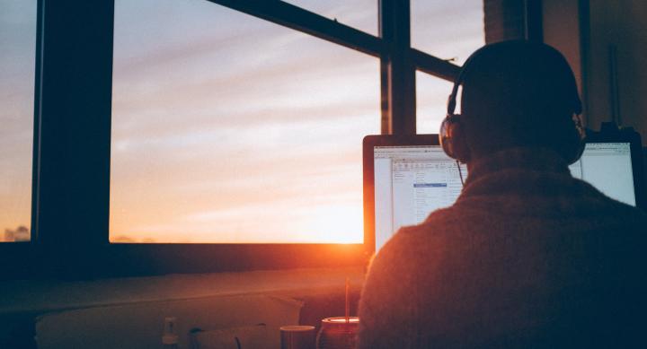 Man at desk with headset in front of computer with sunrise in window
