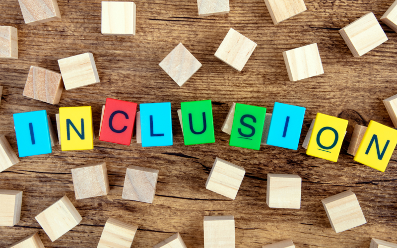 An image of a collection of brightly colored wooden blocks that spell out "inclusion" surrounded by plain wooden blocks 