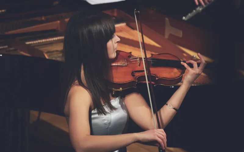 Woman practicing with a violin next to a grand piano.