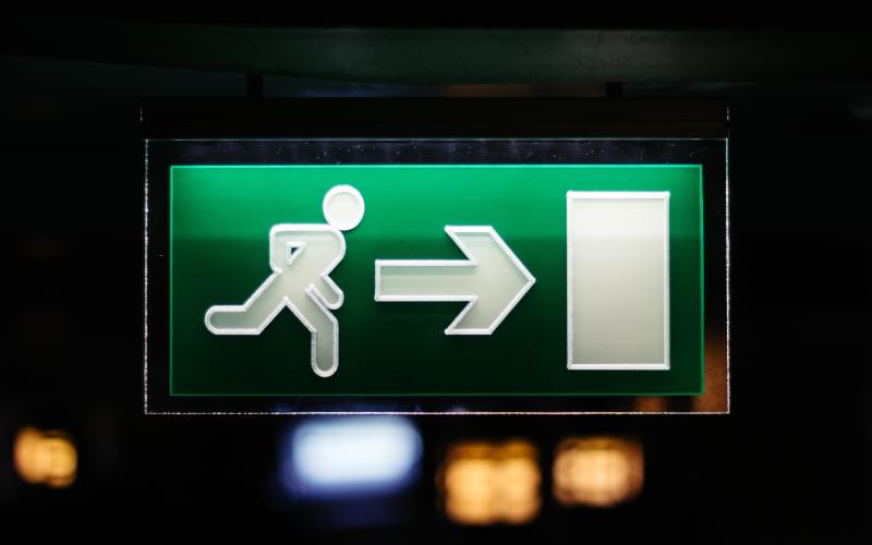 A sign depicts a person followed by an arrow pointing at a door, visually communicating the message that the person should go through the door.