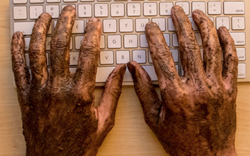 hands covered in mud typing on a keyboard.